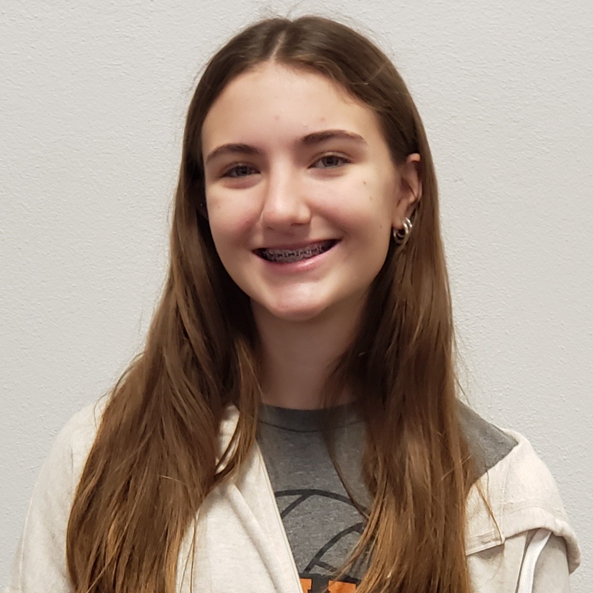 young lady with long brown hair wearing a gray t-shirt under a cream zipped-up jacket