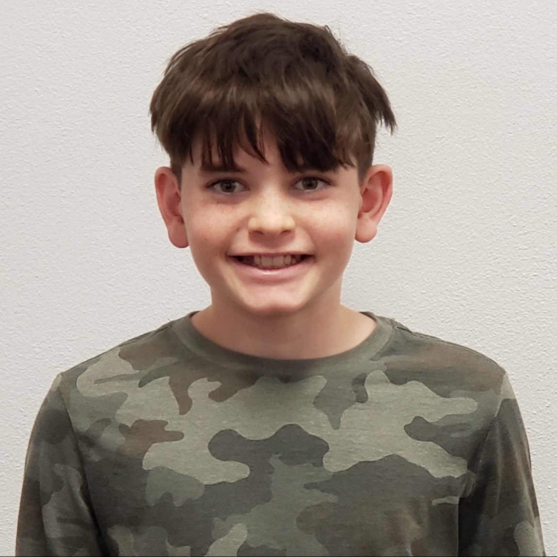 smiling boy with dark hair and freckles wearing a green camouflage t-shirt