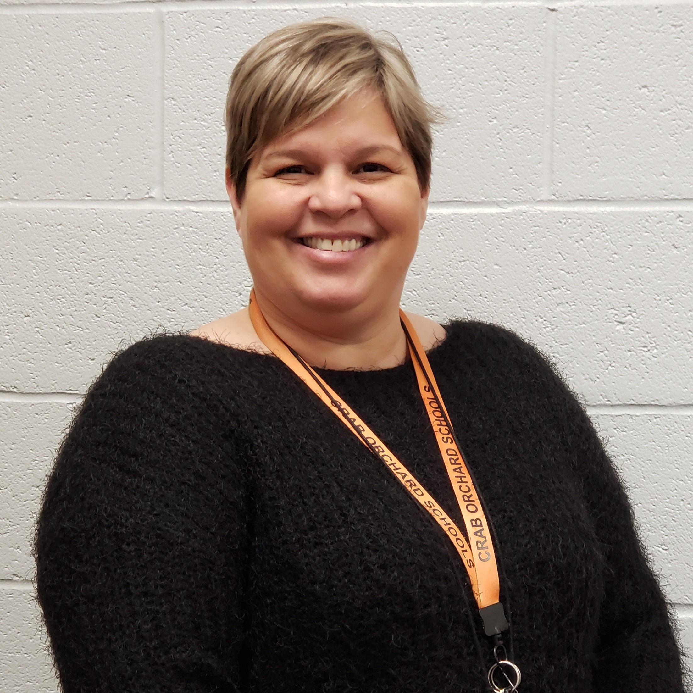 female staff member with short blonde hair wearing a black sweater and an orange lanyard