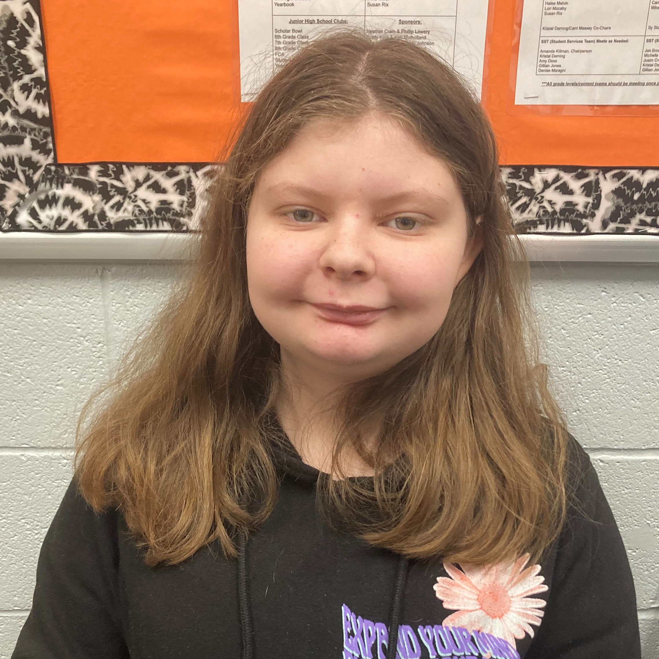 junior high female with light brown hair wearing a black hoodie with a pink flower in the left hand corner