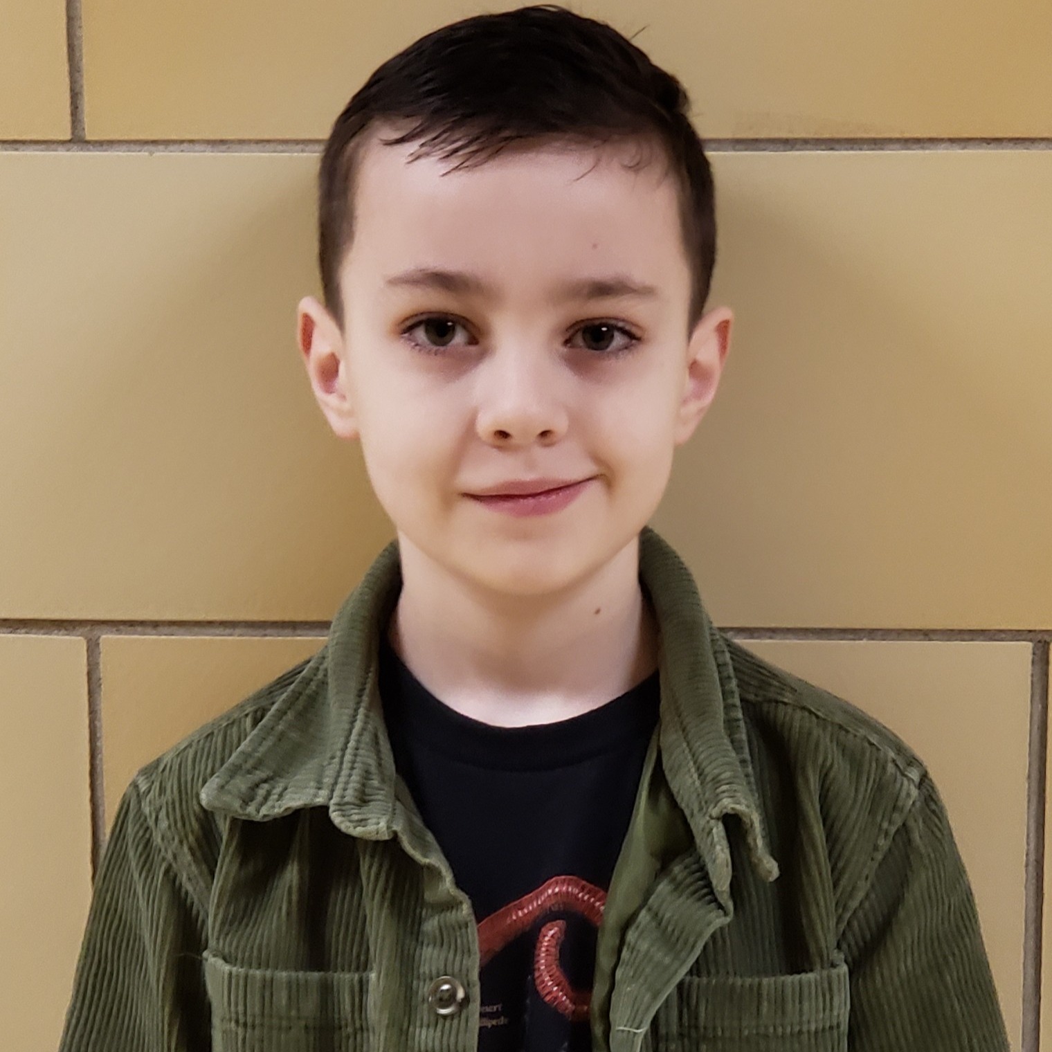 smiling young boy with brown hair wearing a black t-shirt under a green corduroy 