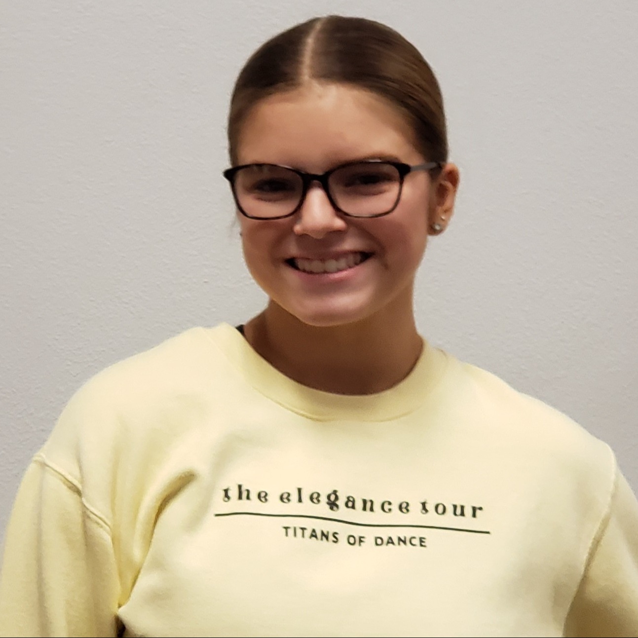 smiling young lady with brown hair pulled back and glasses wearing a light yellow sweatshirt