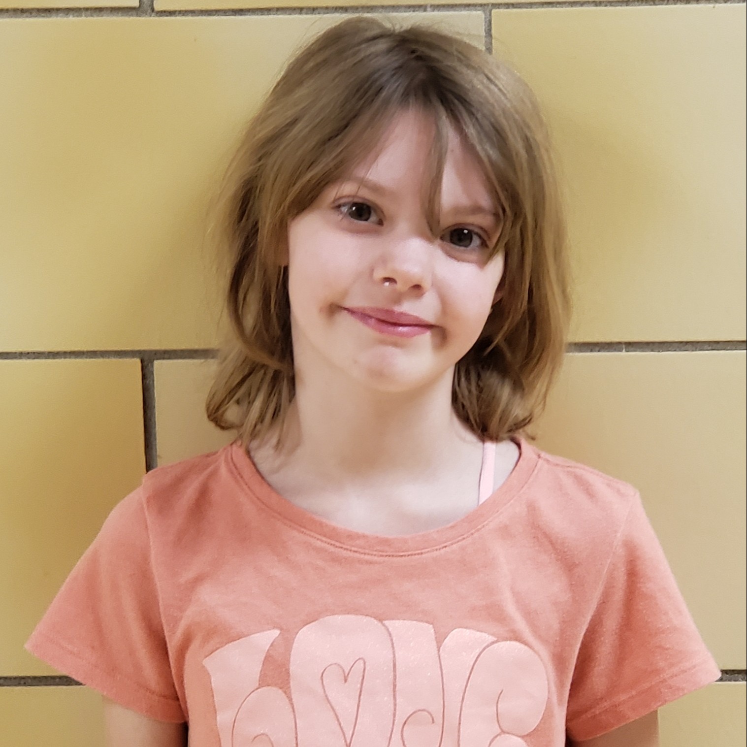 smiling young girl with dark blonde hair wearing a pink t-shirt