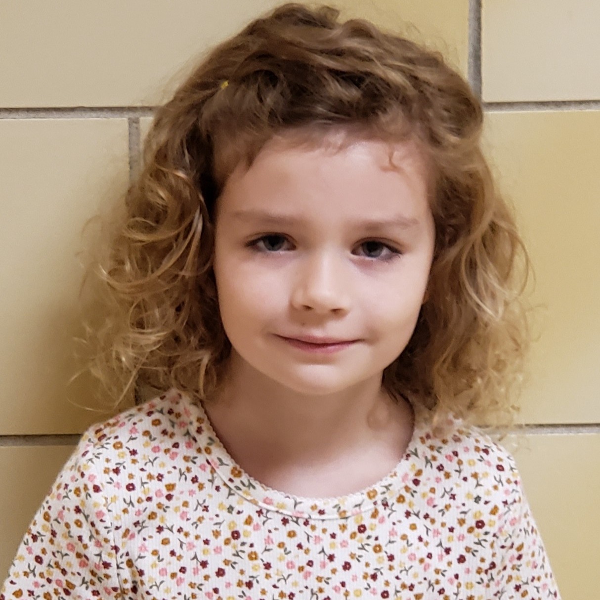 young girl with curly blonde hair wearing a white  t-shirt covered in tiny flowers