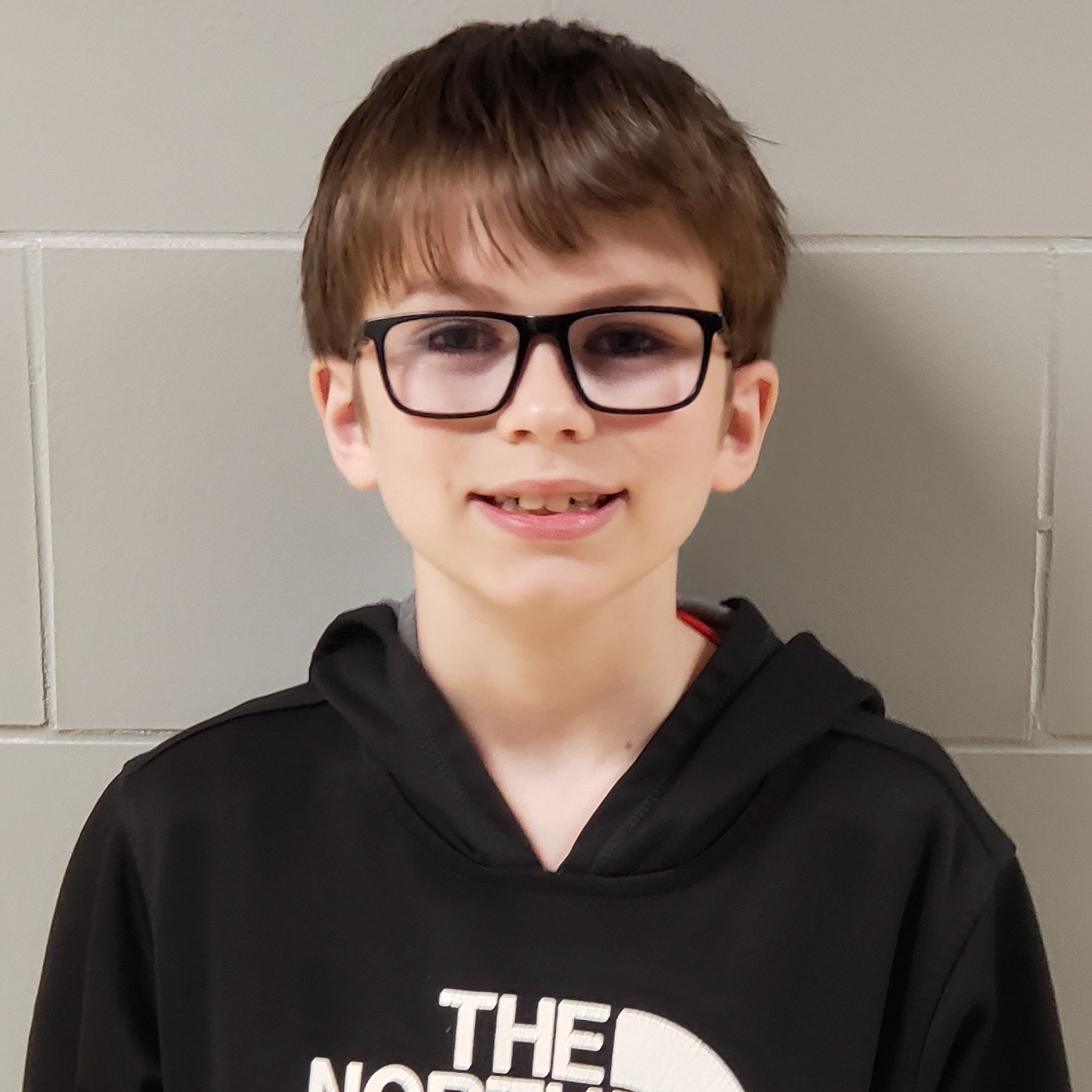 smiling boy with dark hair and black glasses wearing a black hooded sweatshirt