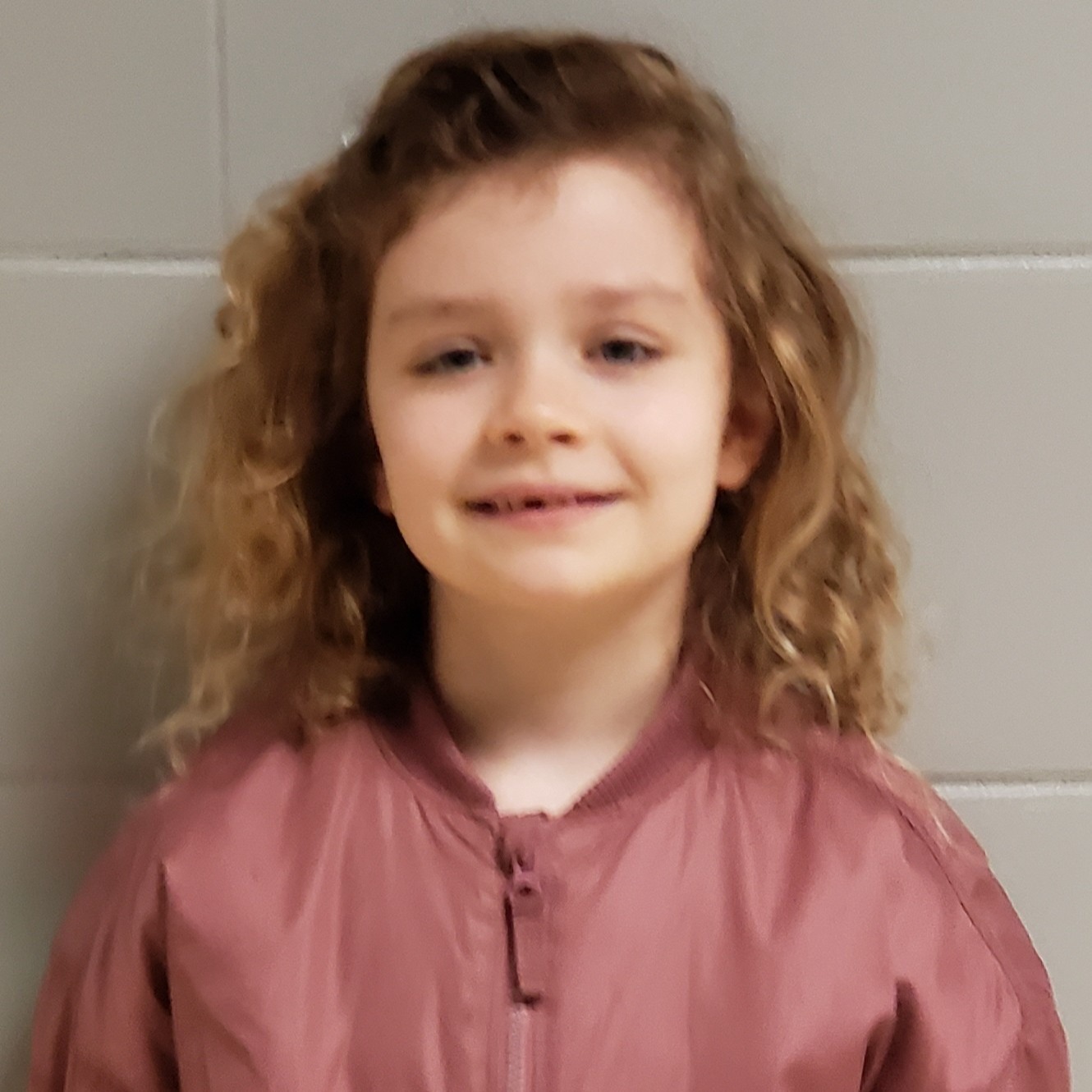 smiling young girl with curly hair wearing a mauve zipped up jacket