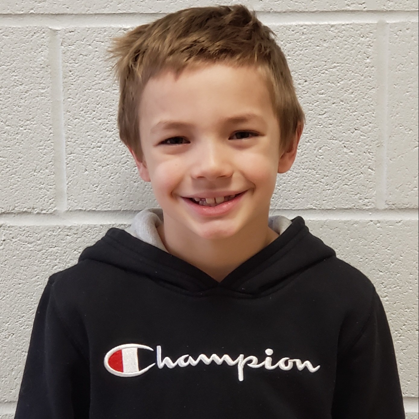 smiling young boy with dark blonde hair wearing a black Champion hooded sweatshirt