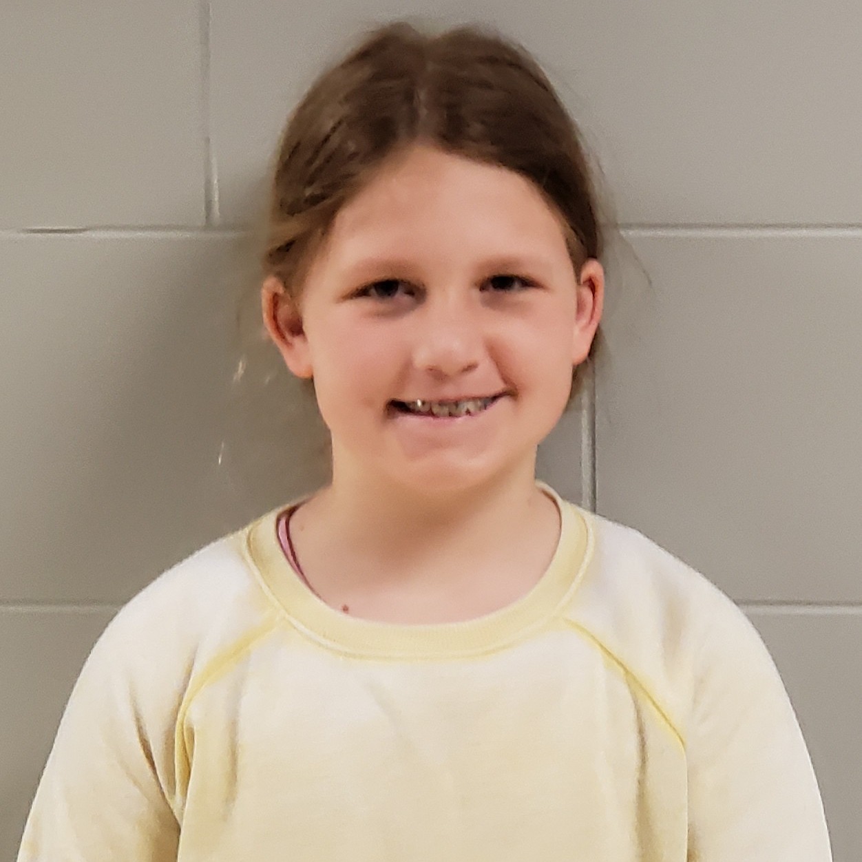 smiling young girl withbraces and  light brown hair pulled back wearing a yellow sweatshirt 