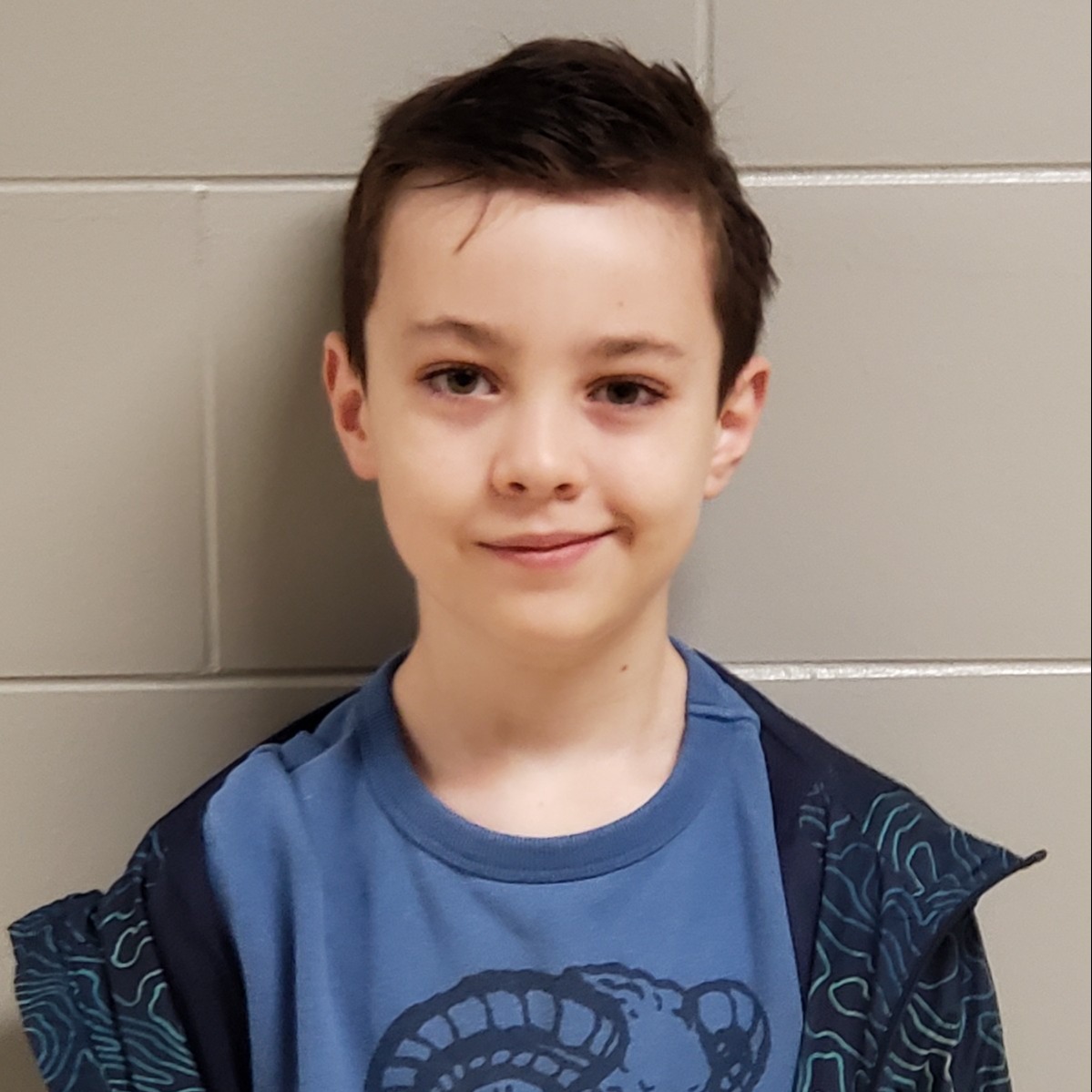 young boy with dark hair wearing a blue t-shirt under a dark blue jacket with light blue swirls