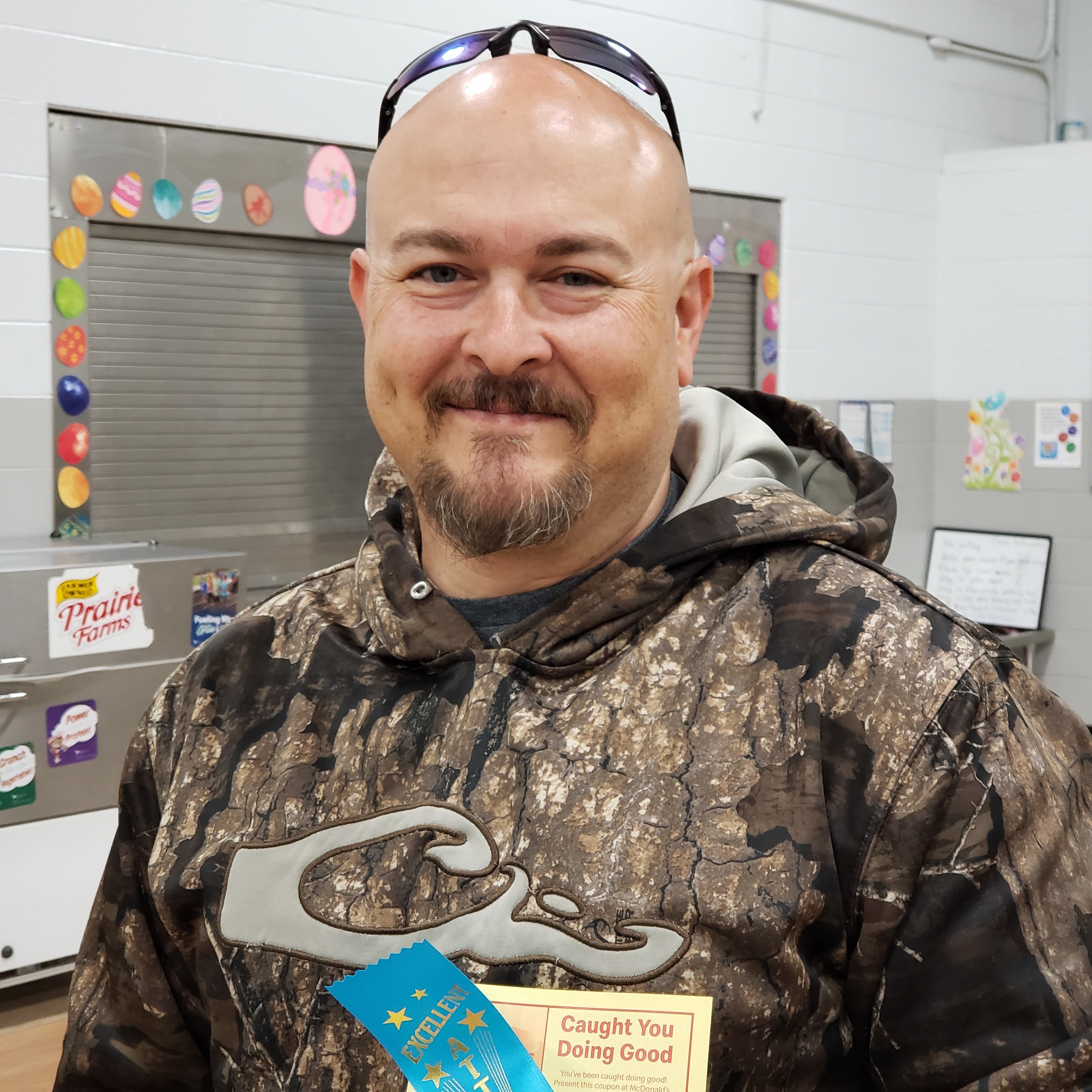 smiling bald man with goatee and sunglasses on his head wearing a camouflage hooded sweatshirt