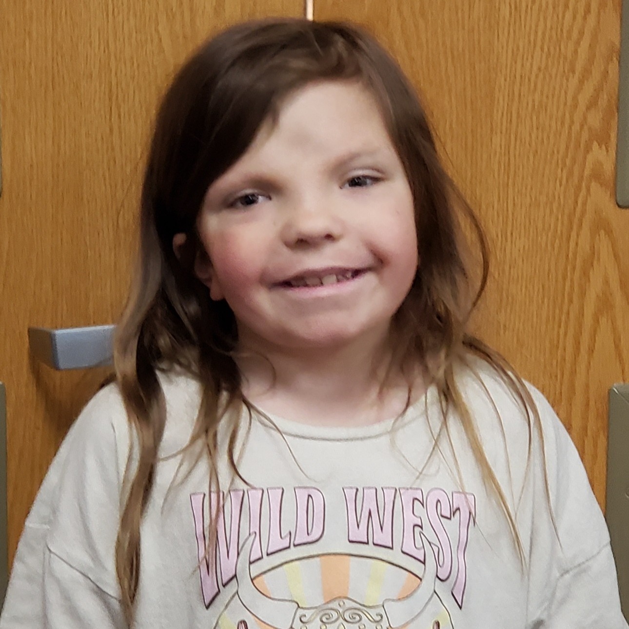 smiling young girl with brown hair wearing a tan WILD WEST t-shirt