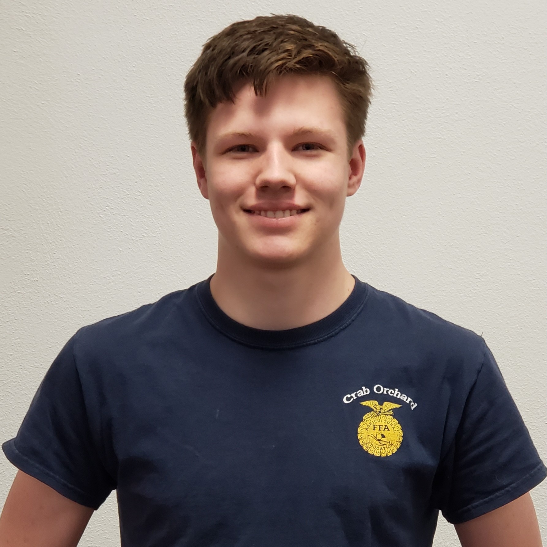 smiling young man with brown hair wearing a navy Crab Orchard FFA t-shirt