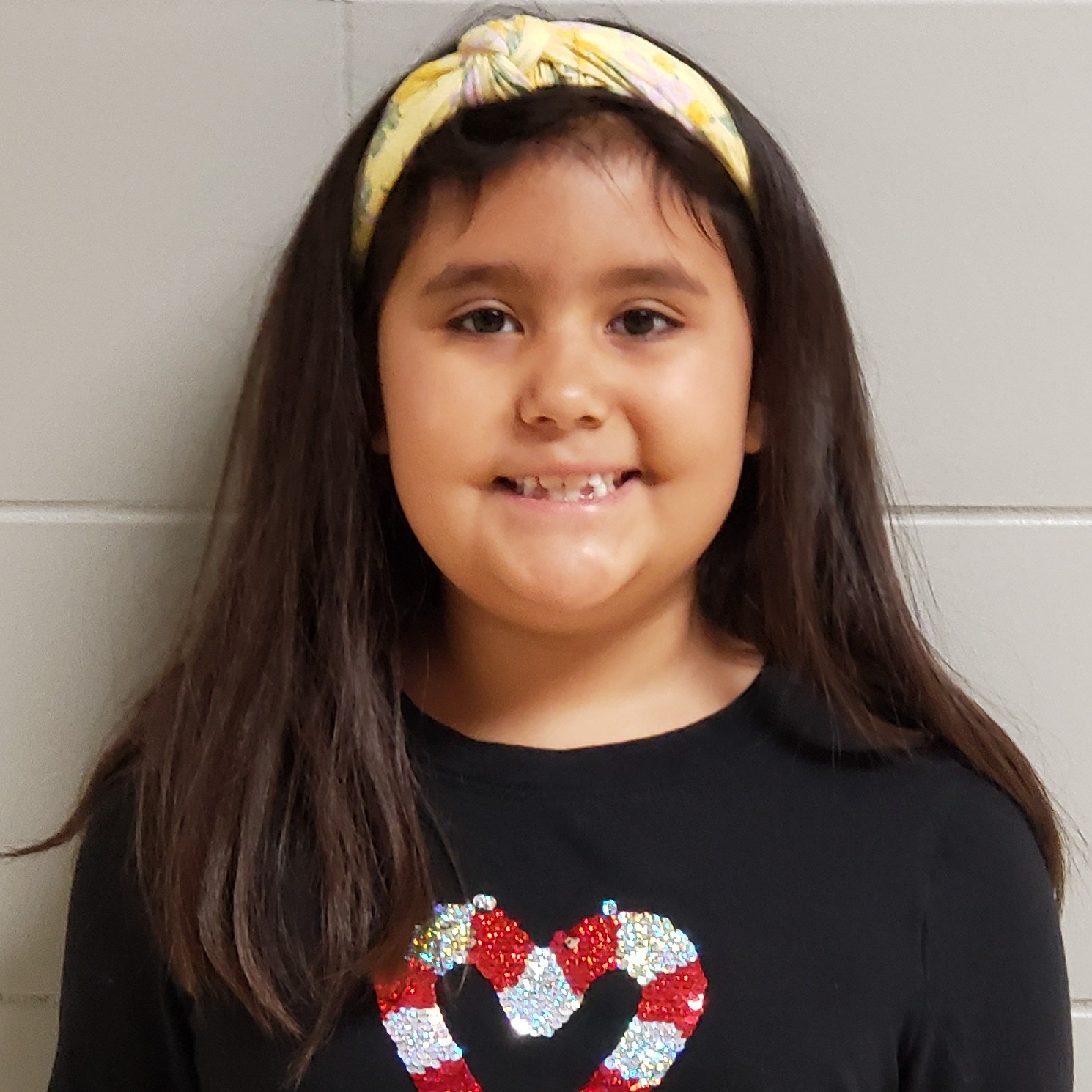 smiling girl with long brown hair wearing a black t-shirt with a candy cane heart on it and a yellow headband