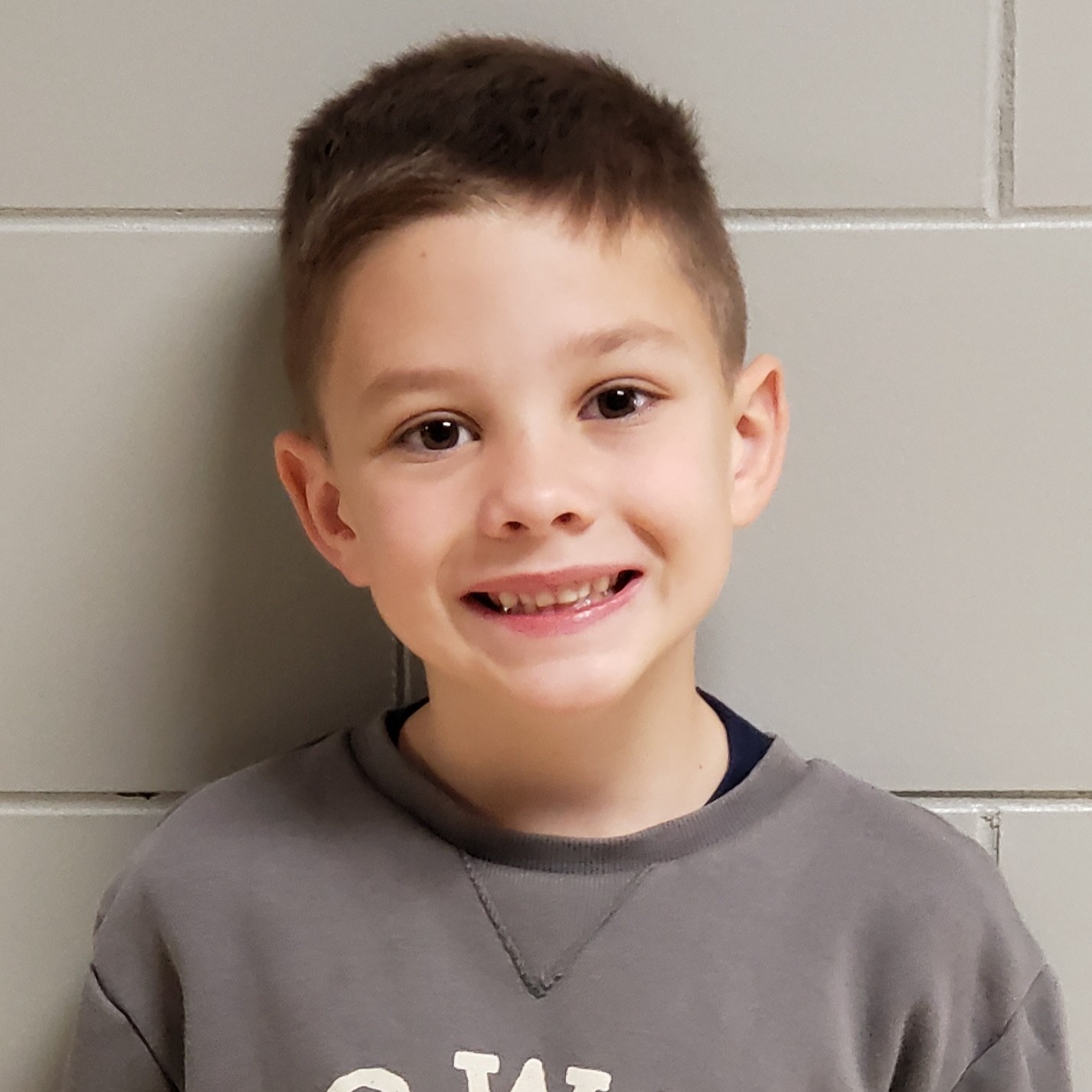 smiling boy with dark blonde hair wearing a gray sweatshirt