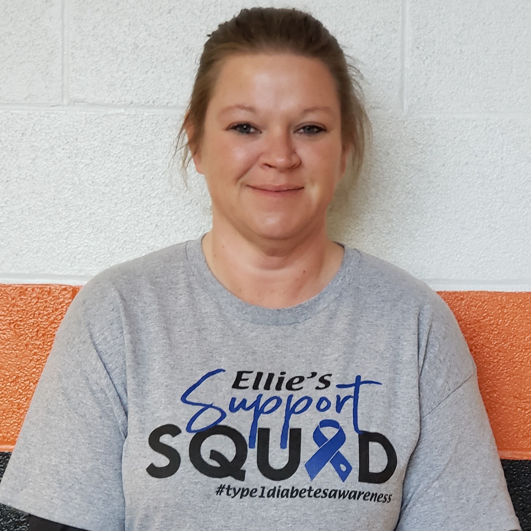 female staff member with dark blonde hair pulled back wearing a gray Ellie's Support Squad t-shirt
