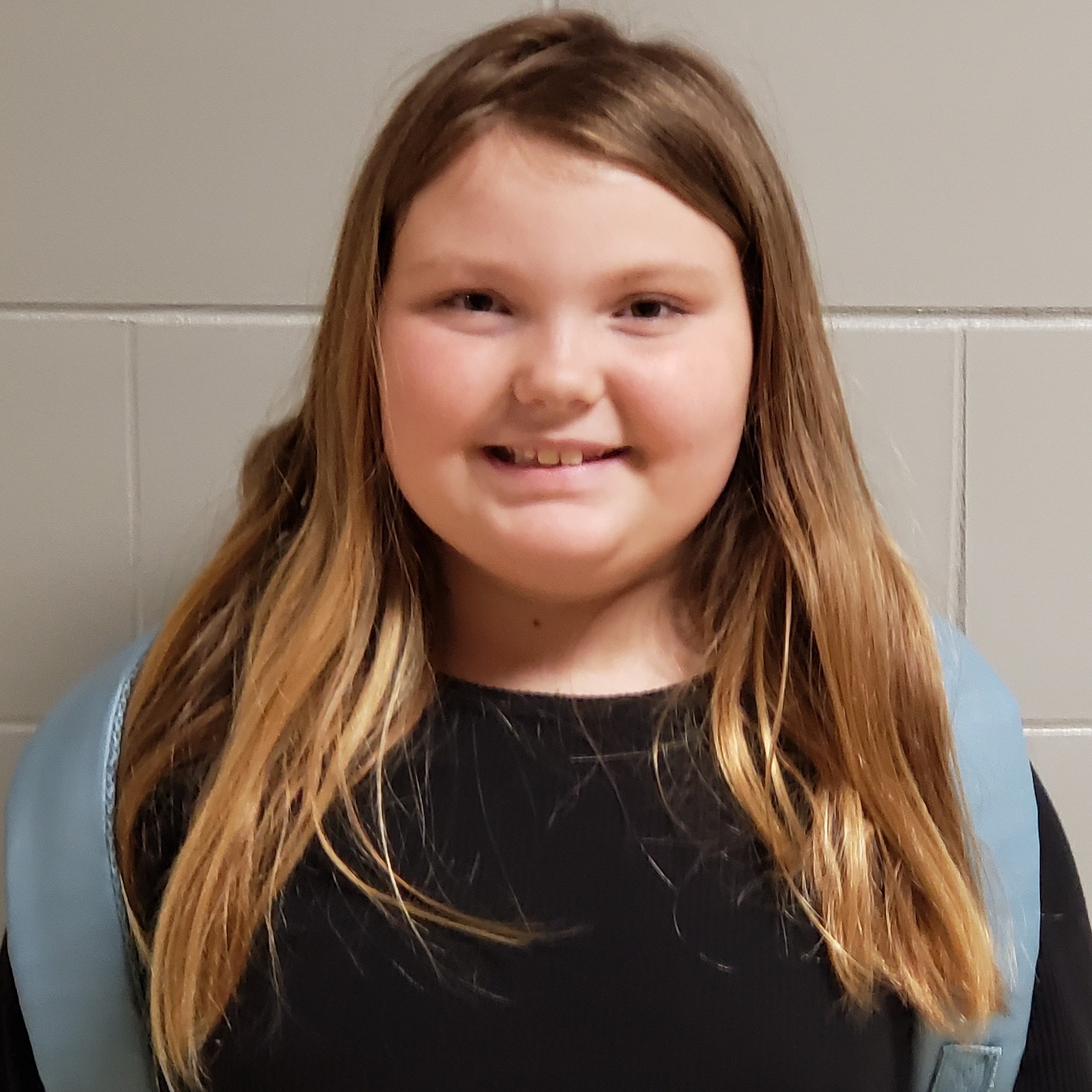 smiling young girl with long dark blonde hair wearing a black t-shirt and blue backpack