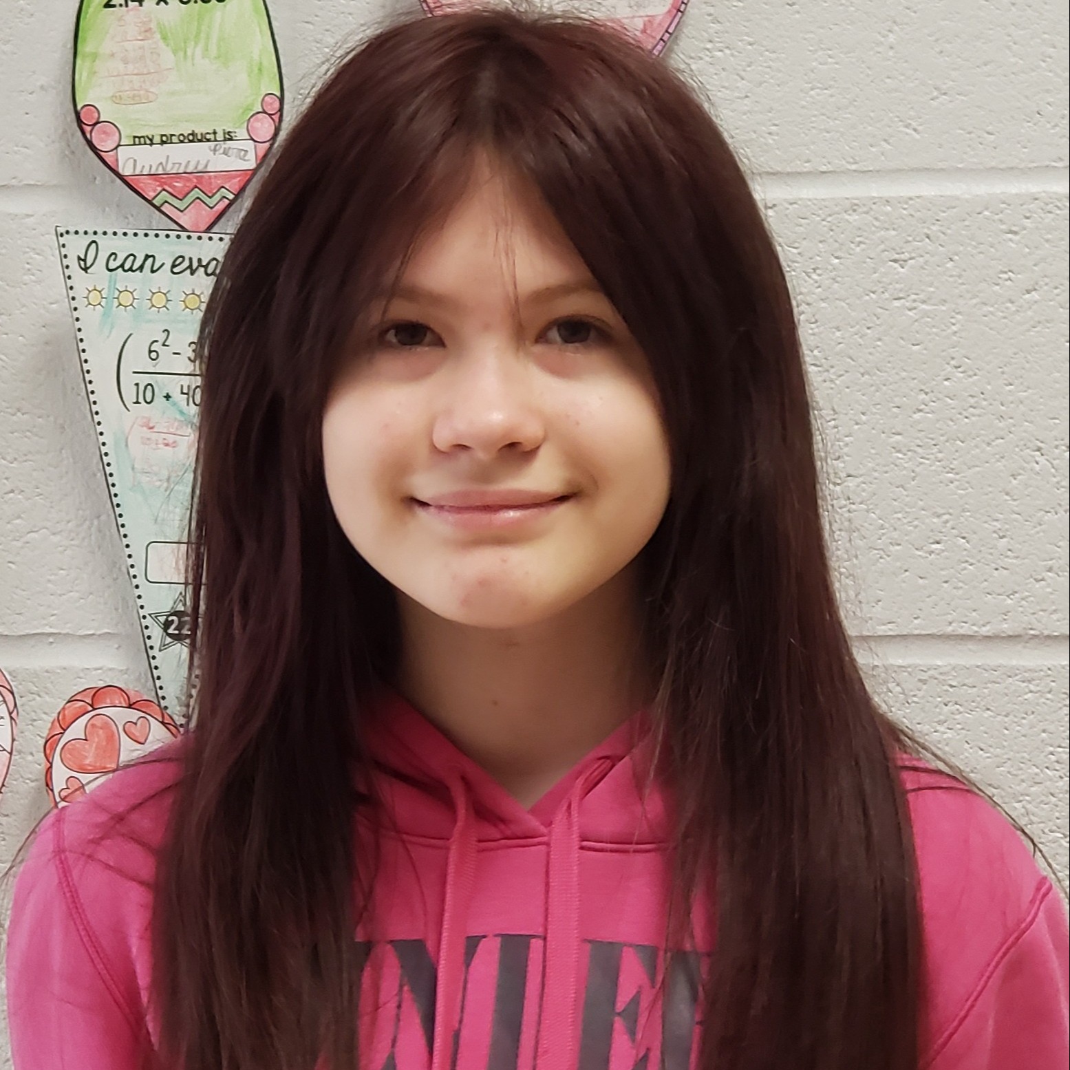 smiling girl with long reddish brown hair wearing a hot pink hooded sweatshirt