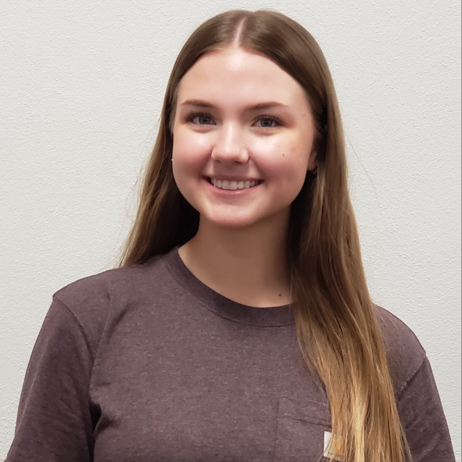 smiling young lady with long golden blonde hair wearing a  heather maroon t-shirt