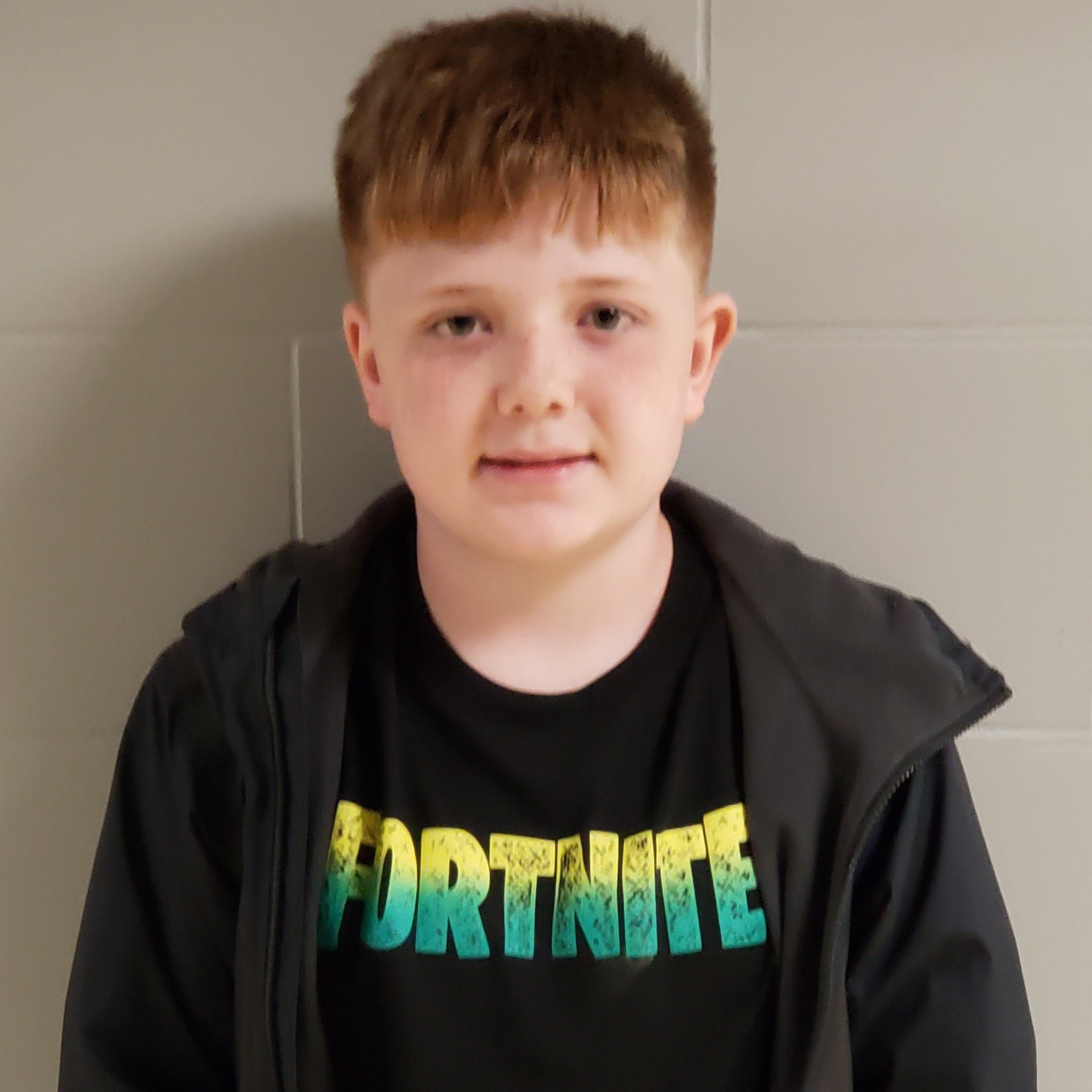boy with reddish hair and freckles wearing a black FORTNITE t-shirt under a dark gray jacket