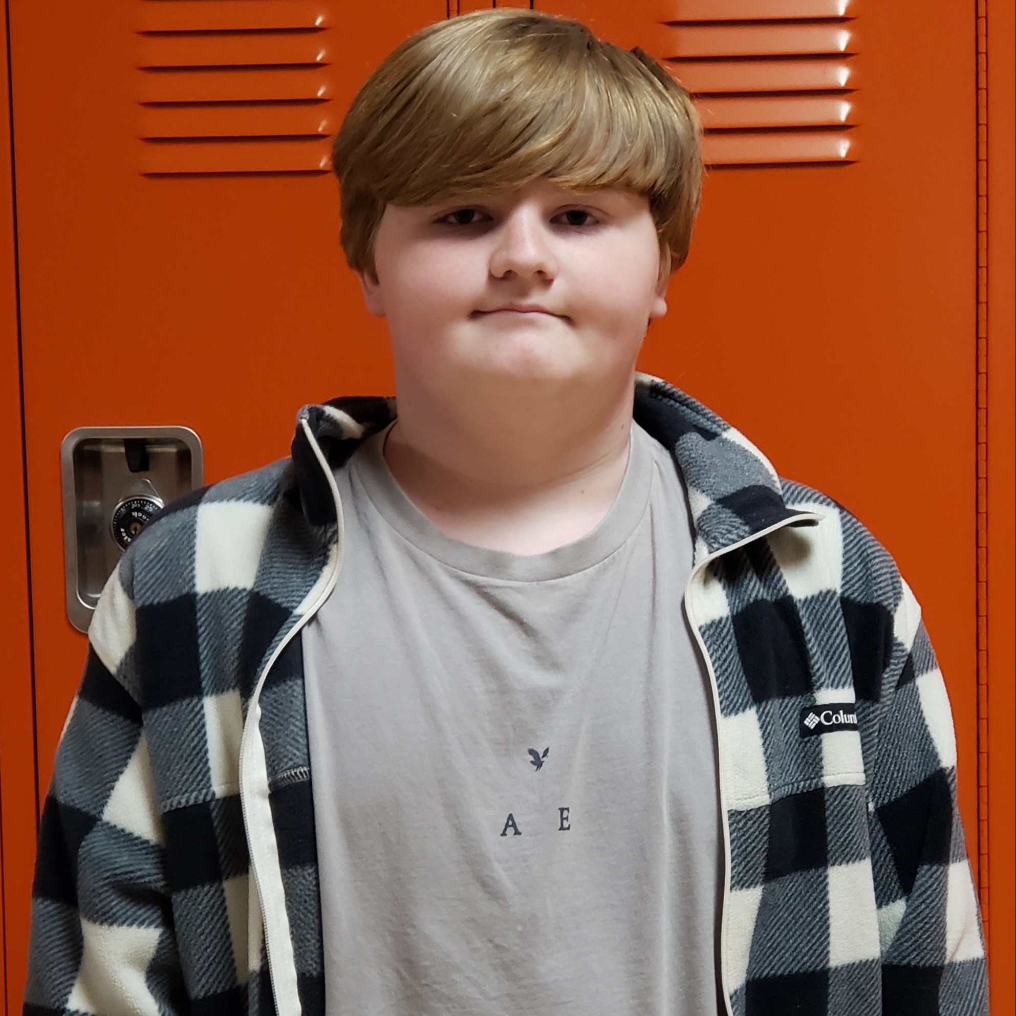 boy with reddish hair wearing a gray t-shirt under a black & white plaid jacket