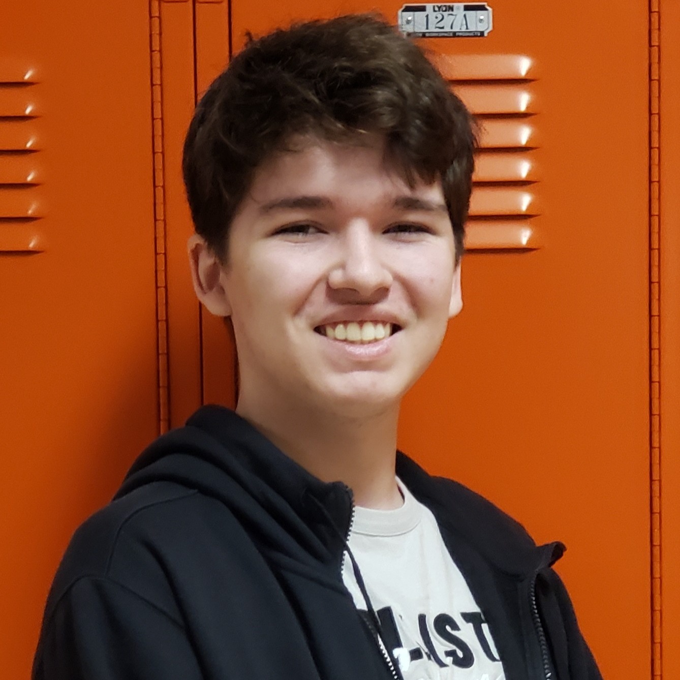 young man with brown hair wearing a gray t-shirt under a black jacket