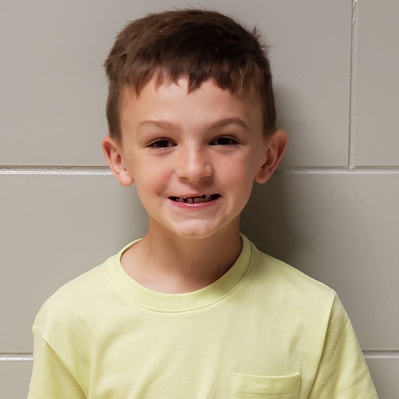 smiling little boy with dark hair wearing a yellow pocket t-shirt