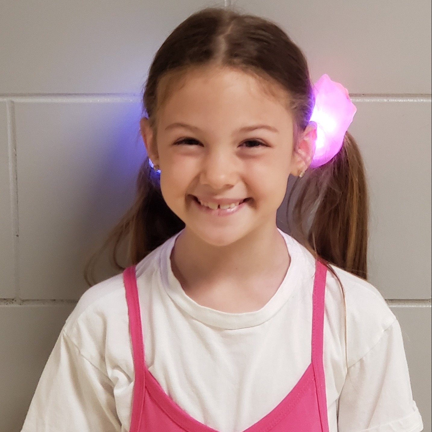 smiling young girl with long dark blonde hair pulled into pigtails with light-up, neon scrunchies