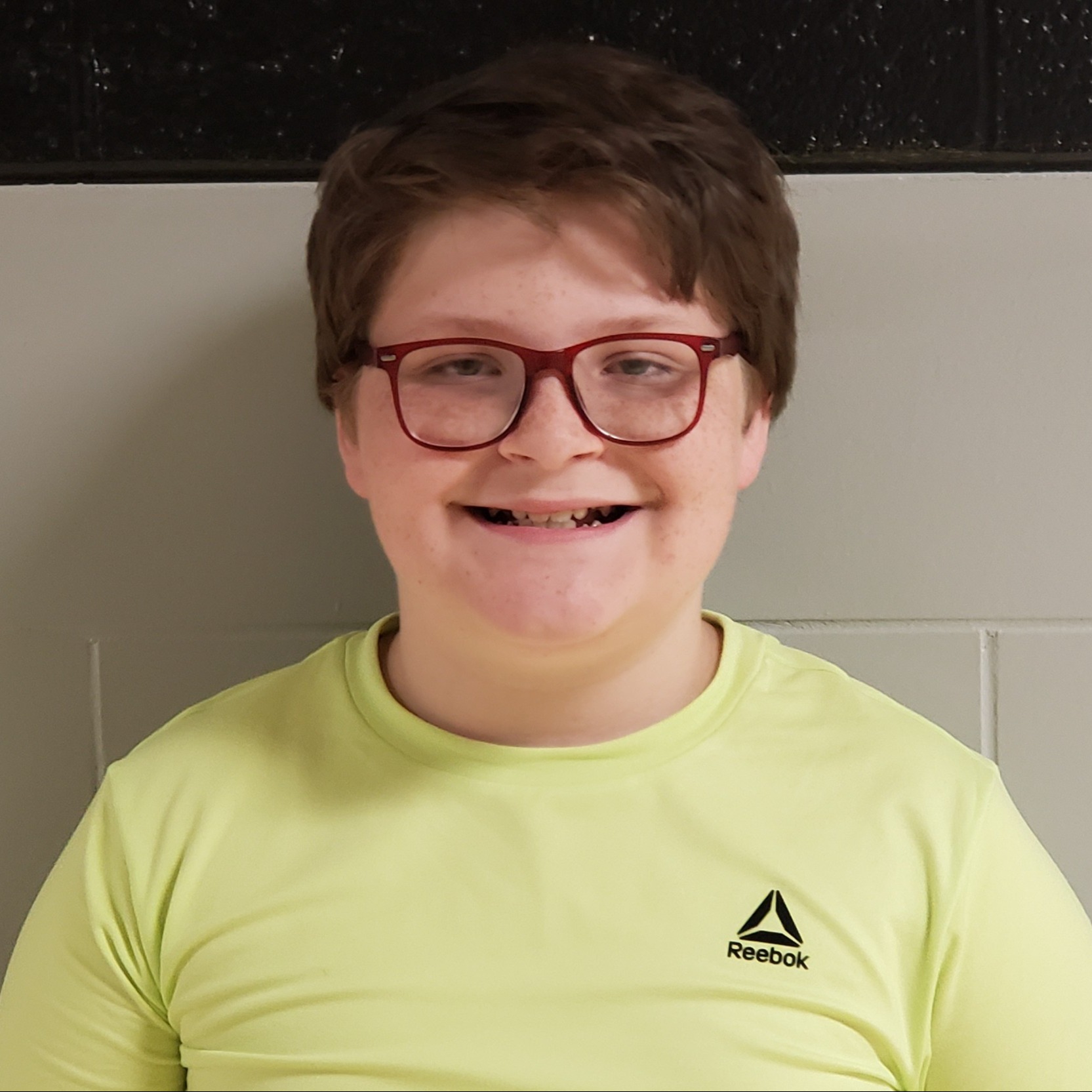 boy with dark hair and red-framed glasses wearing a yellow t-shirt