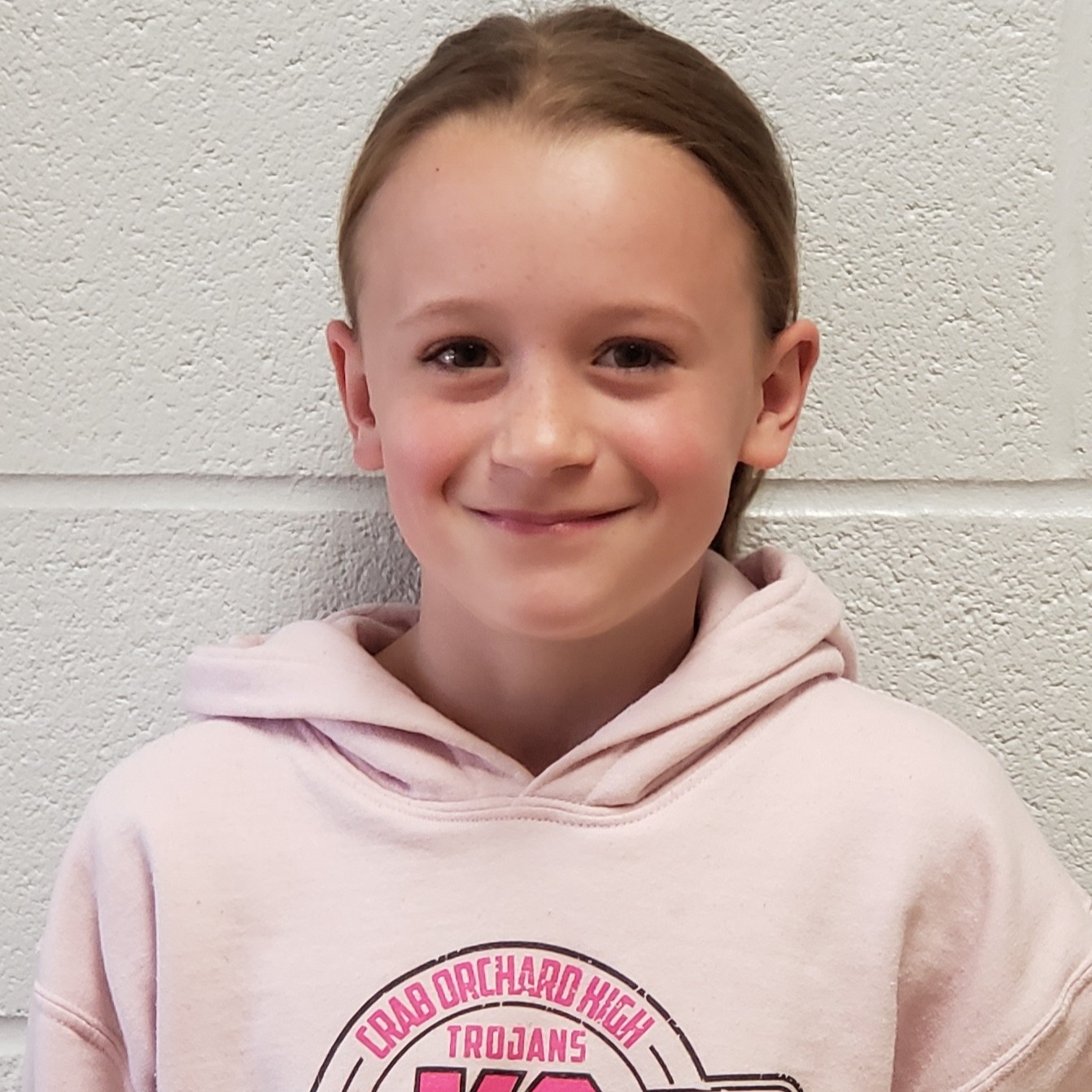 smiling girl with light brown hair pulled back wearing a pink hooded sweatshirt