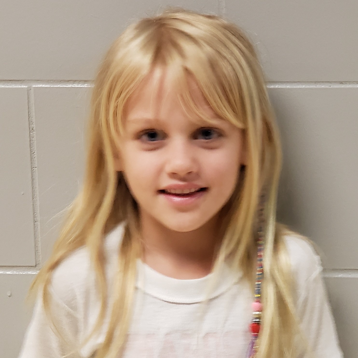 smiling young girl with blonde hair wearing a white t-shirt with beads in her hair