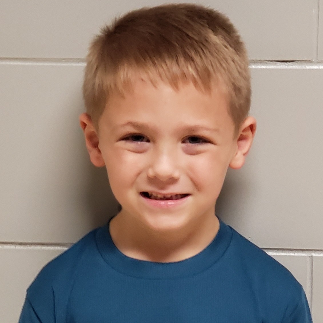 smiling little boy with blonde hair wearing a blue t-shirt