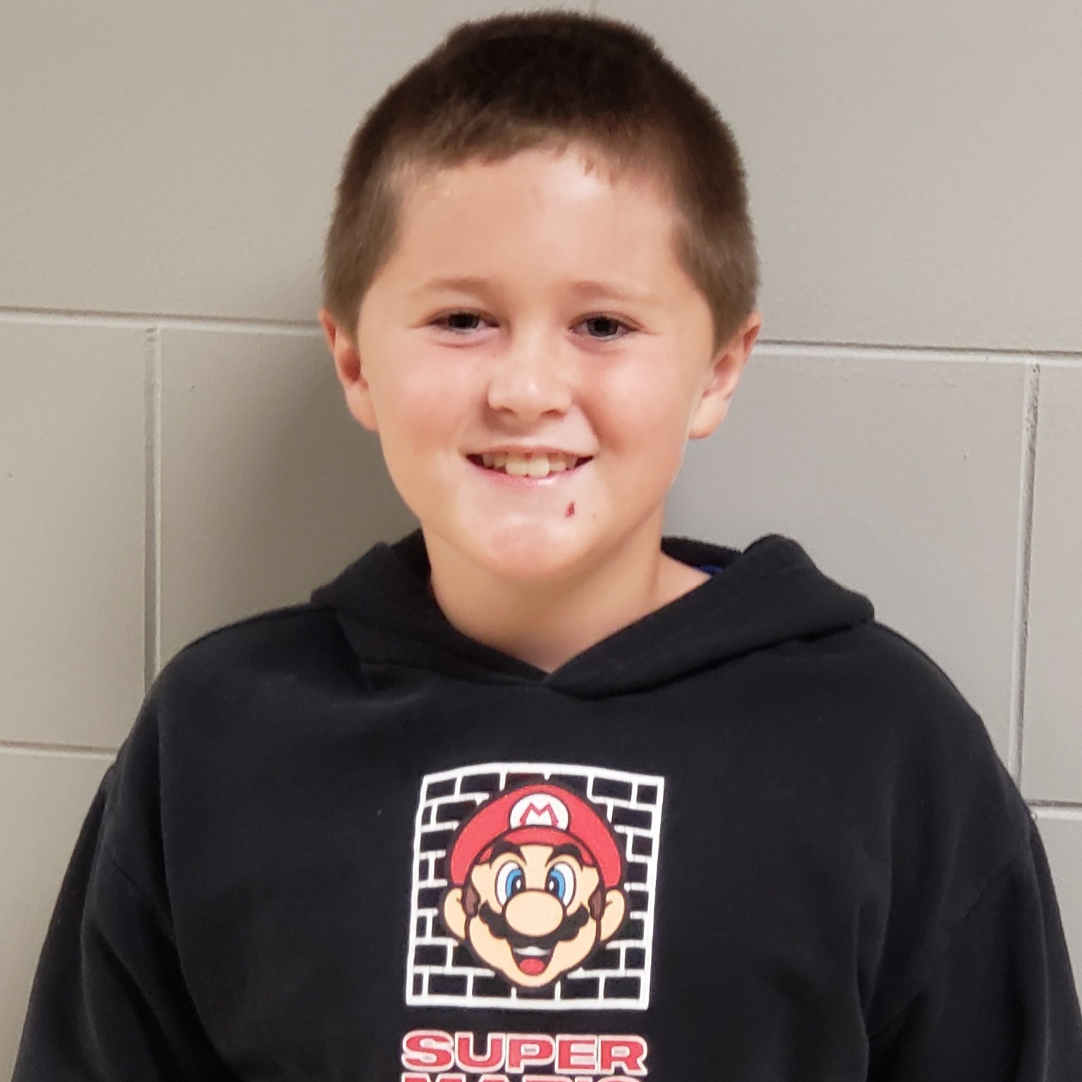 smiling boy with dark blonde hair wearing a black Super Mario hoodie