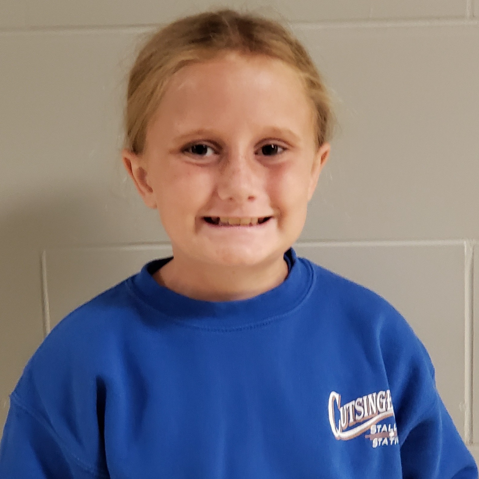 smiling girl with blonde hair pulled back wearing a blue sweatshirt