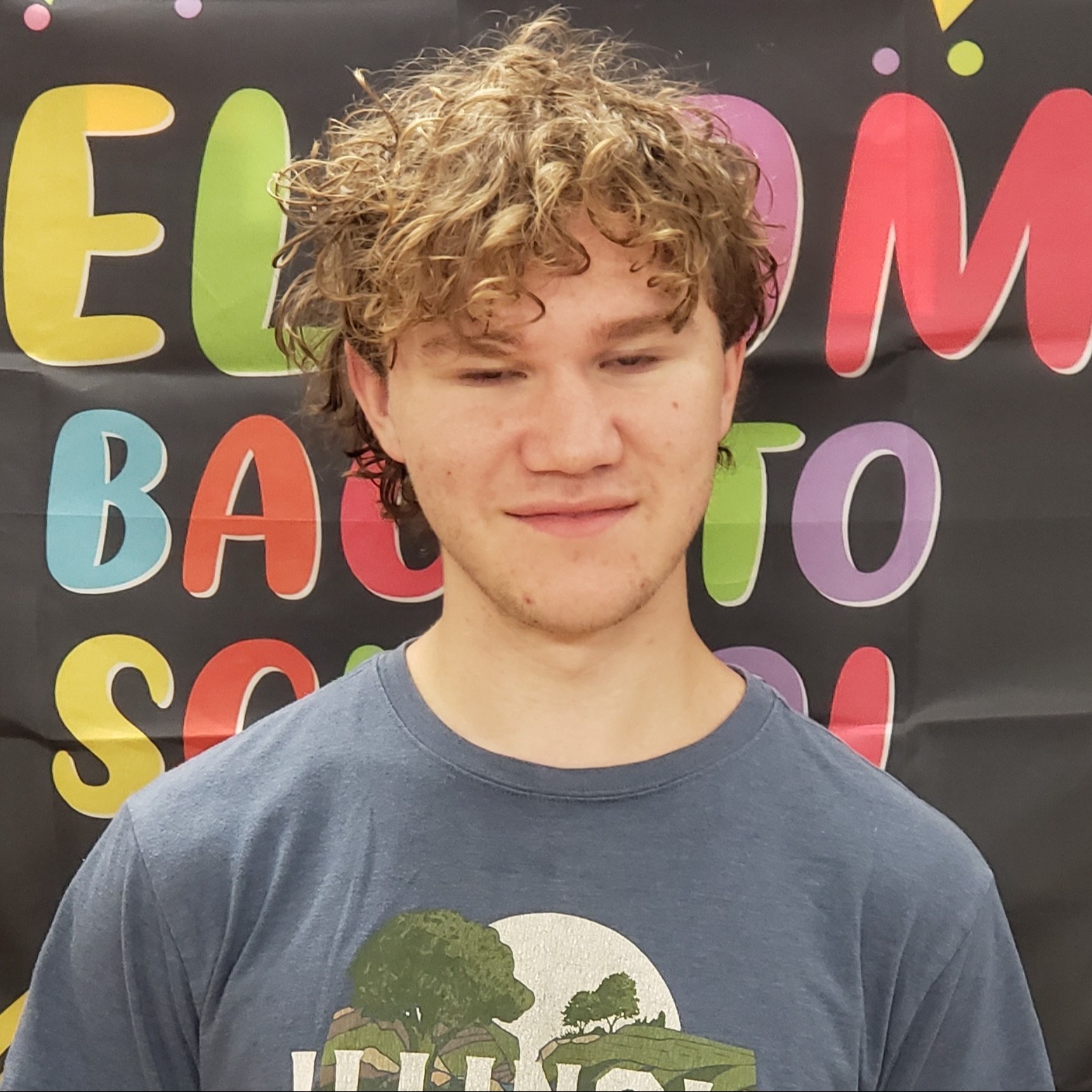 smiling young man with curly brown hair wearing a dark gray t-shirt