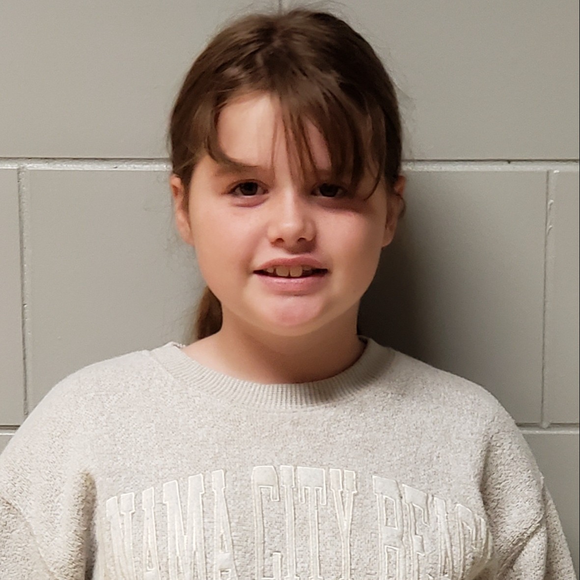 smiling young girl with brown hair pulled back wearing a cream sweatshirt