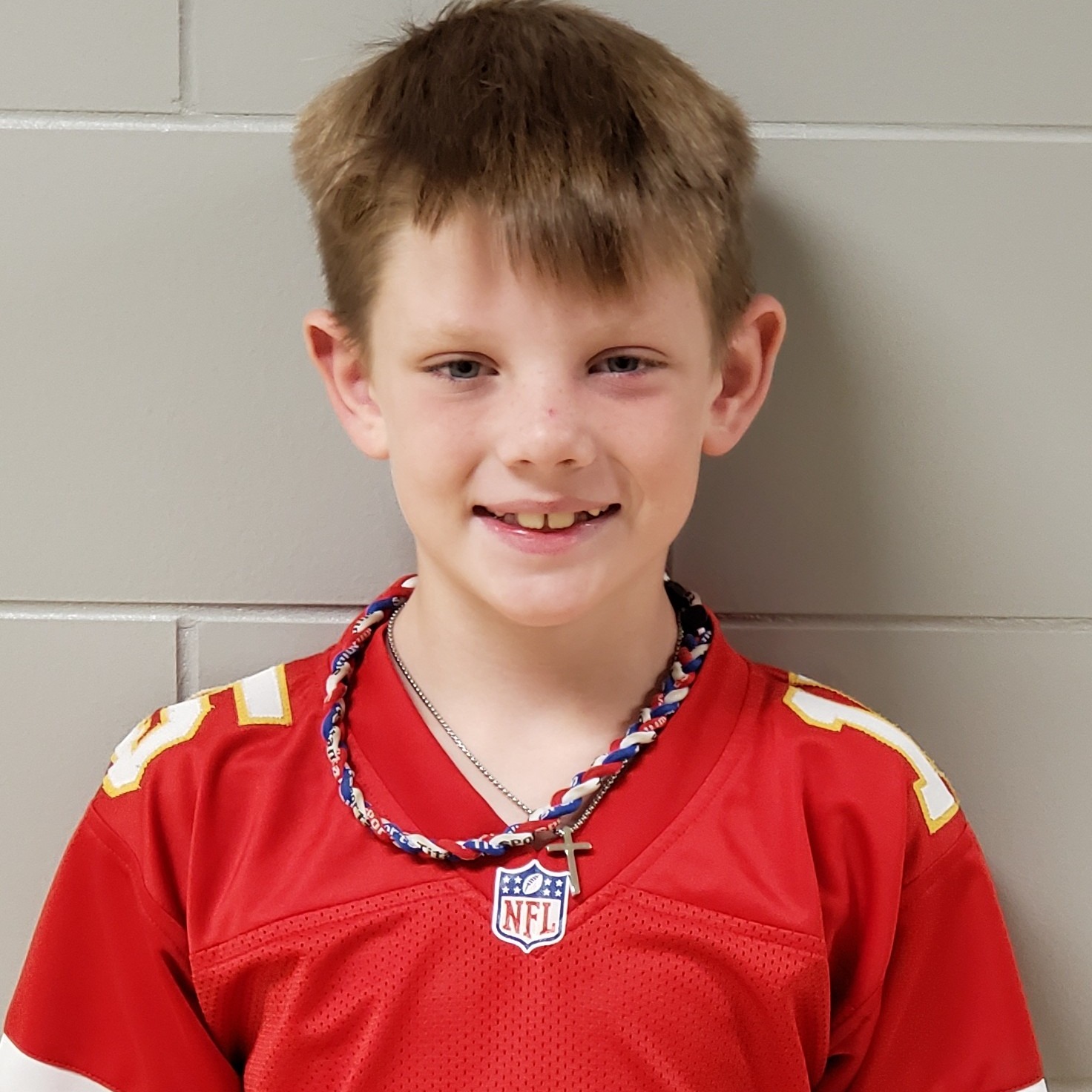 smiling boy with sandy hair wearing a read football jersey