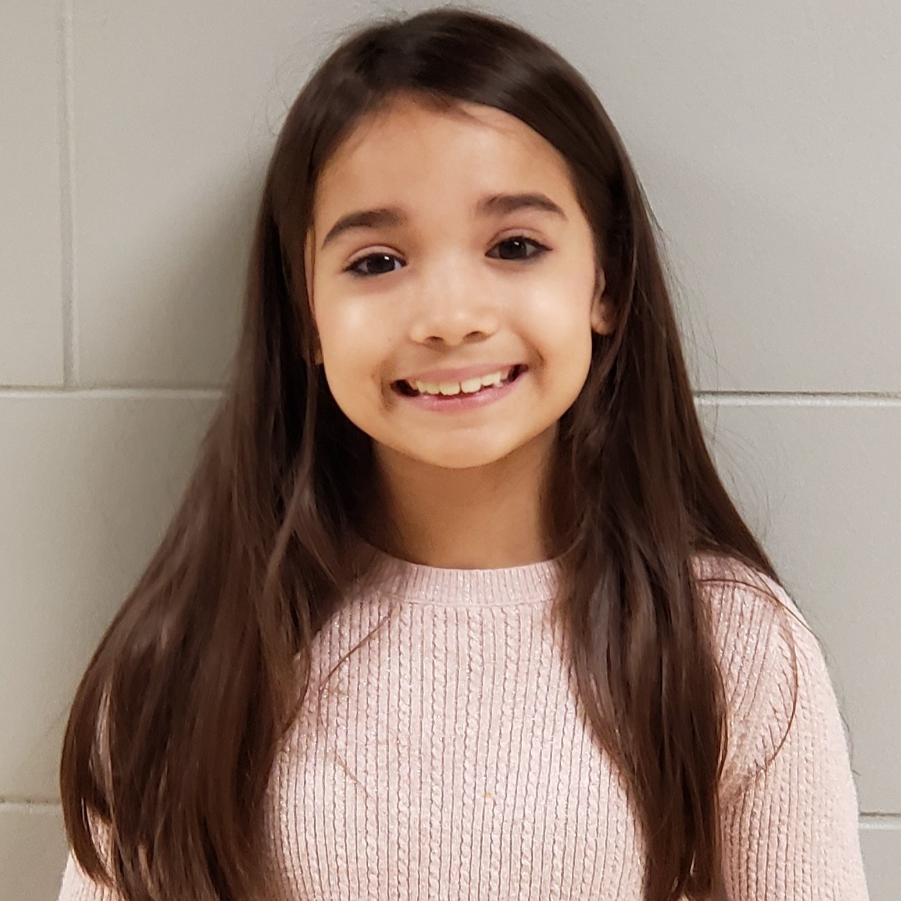 smiling girl with long brown hair wearing a pink sweatercate