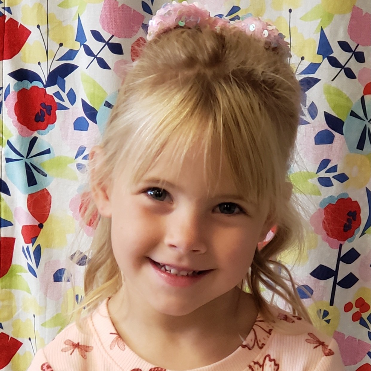 smiling little girl with blonde hair pulled back wearing a pink t-shirt