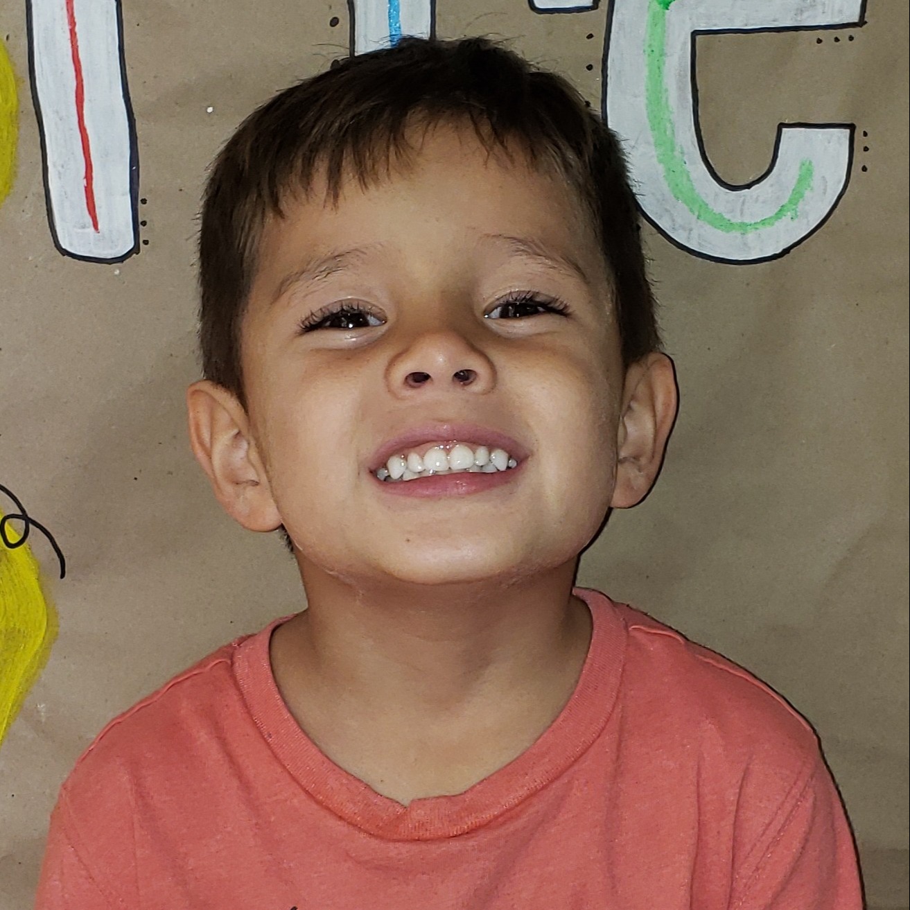 smiling little boy with dark hair wearing a coral t-shirt