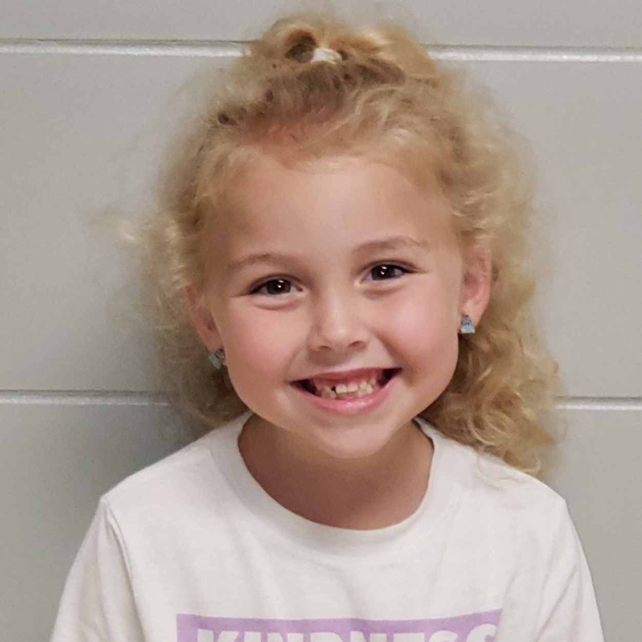 smiling little girl with blonde hair pulled half-up wearing a white t-shirt