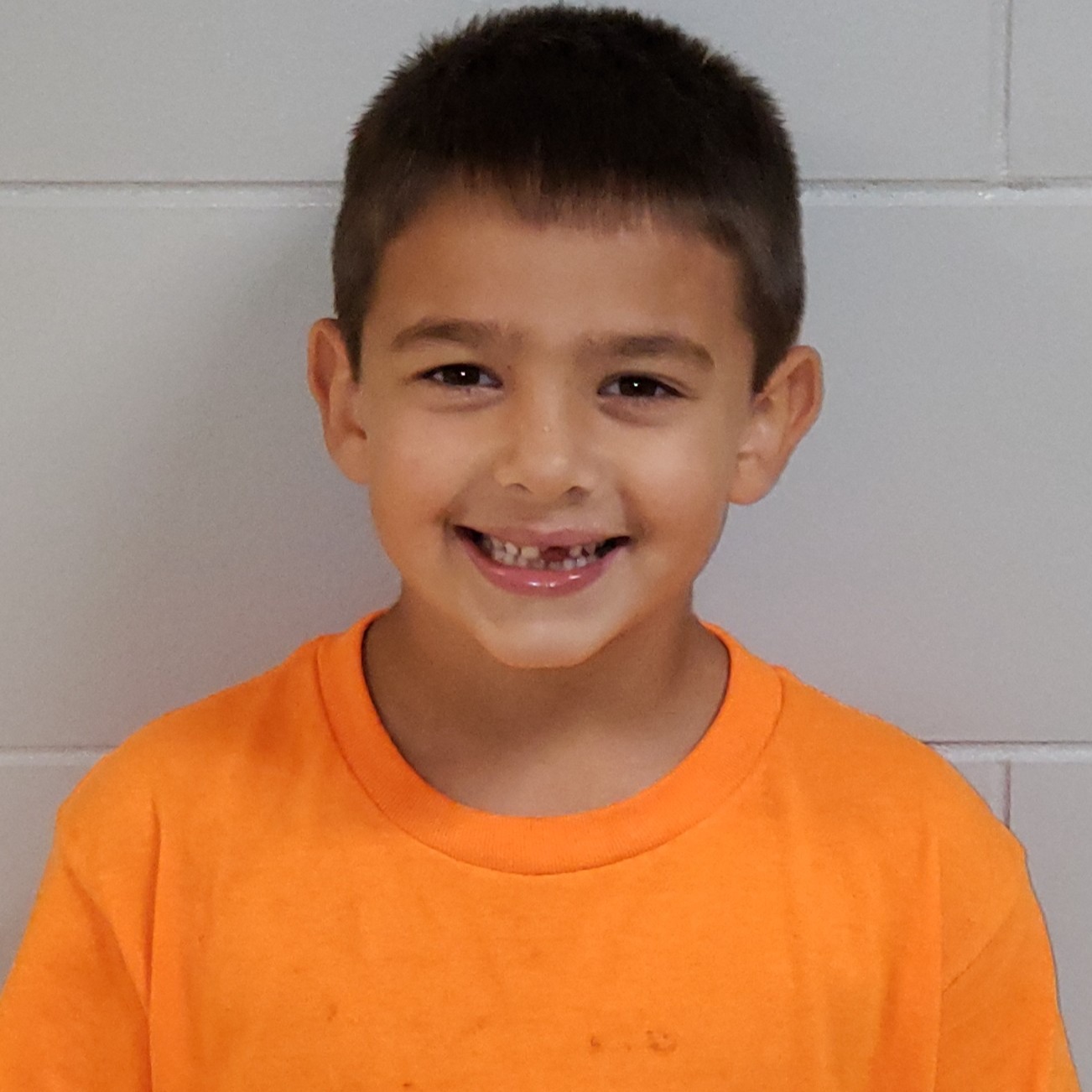 smiling young boy with brown hair wearing an orange t-shirt
