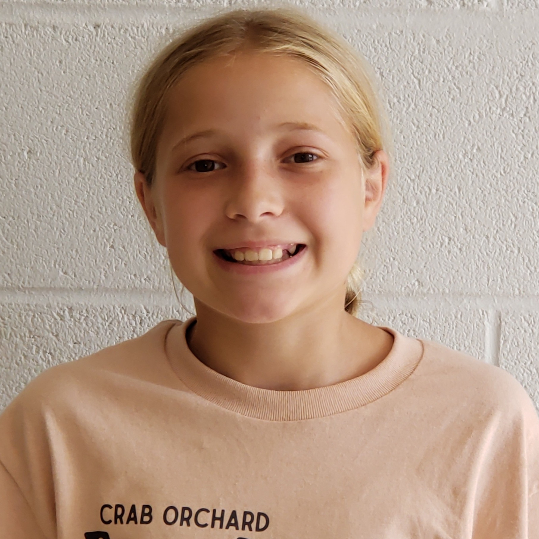 smiling girl with blonde hair pulled back wearing a beige t-shirt