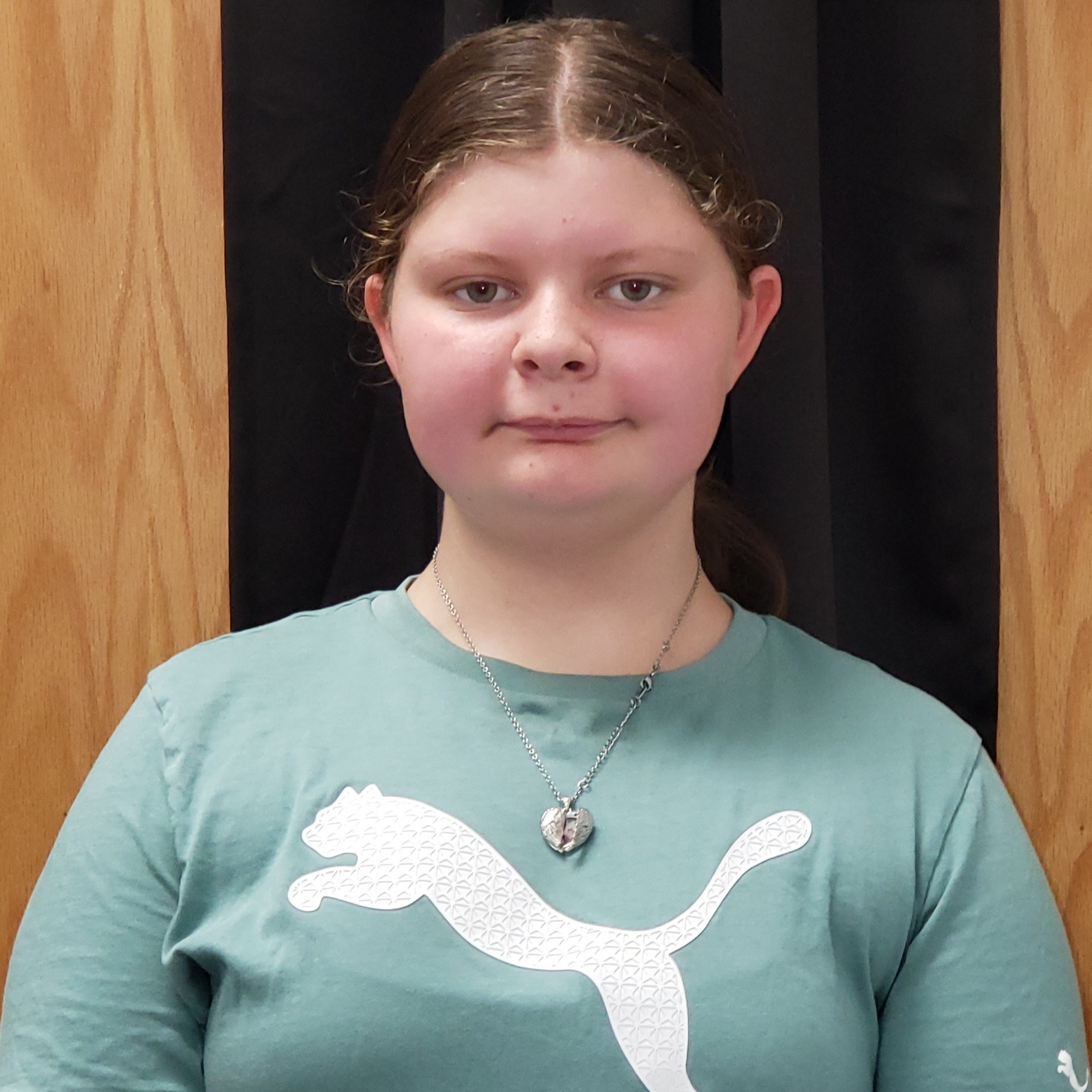 smiling girl with reddish brown  hair pulled back wearing a green puma t-shirt