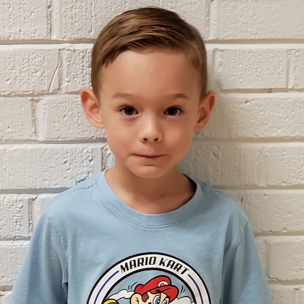 young boy with dark blonde hair wearing a light blue Mario Kart t-shirt