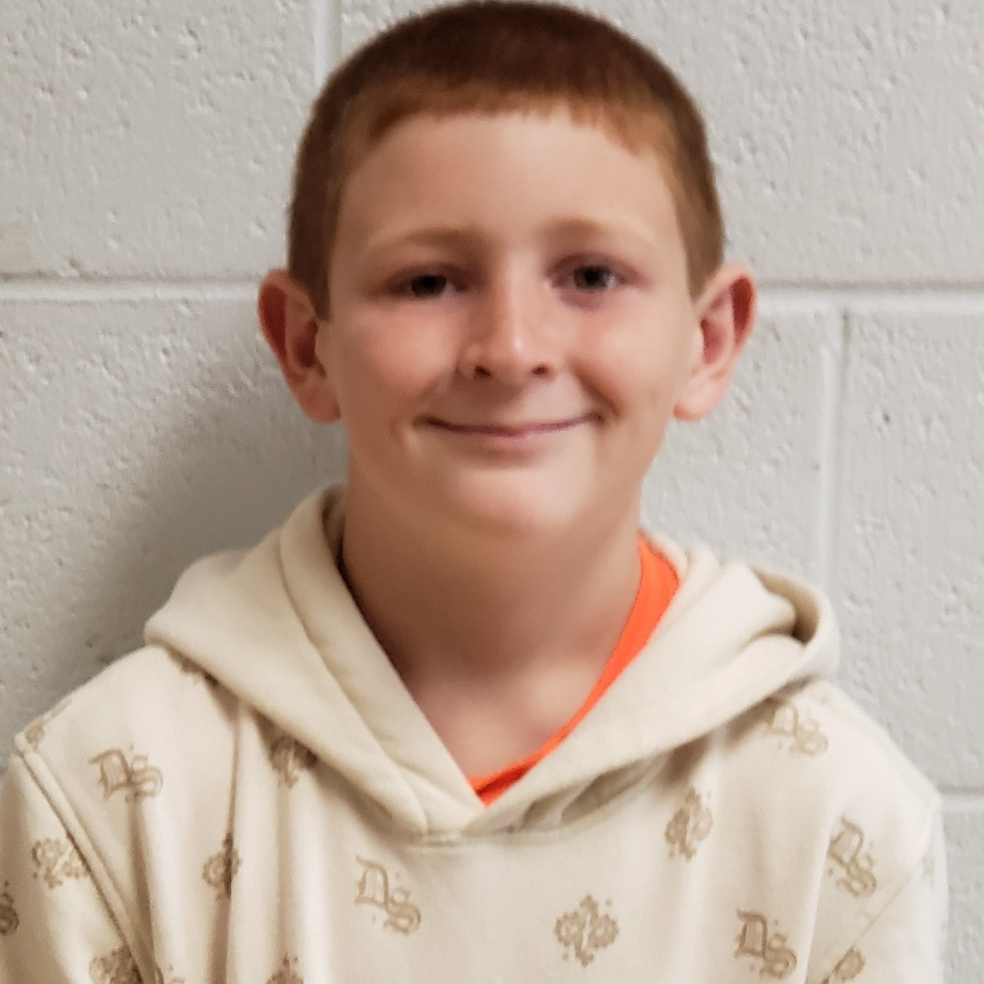 grinning boy with red hair wearing an orange t-shirt under a cream hoodie