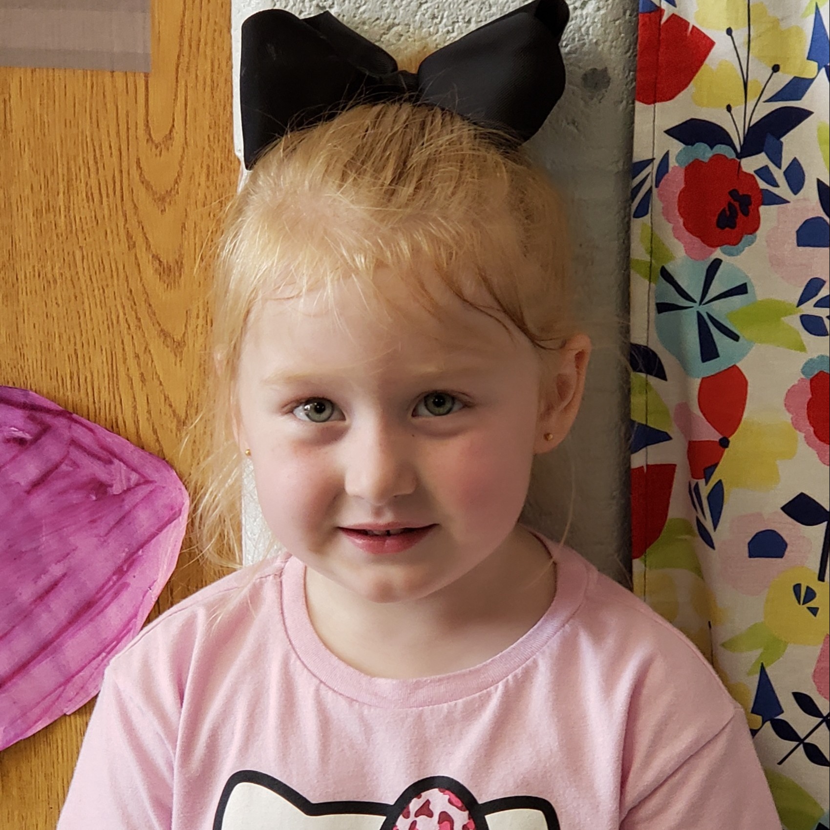 little girl with red hair pulled back in a black bow wearing a pink t-shirt