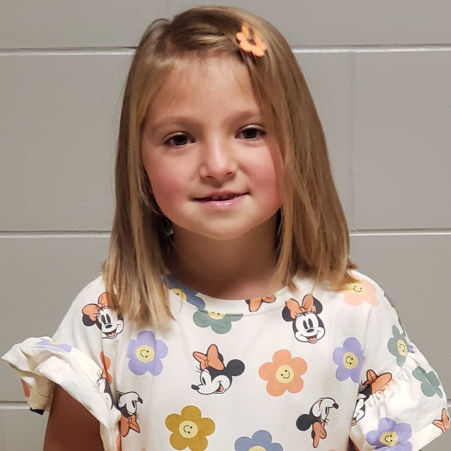 young girl with dark brown hair in an orange barrette wearing a white dress with Minnie Mouse and smiley face flowers