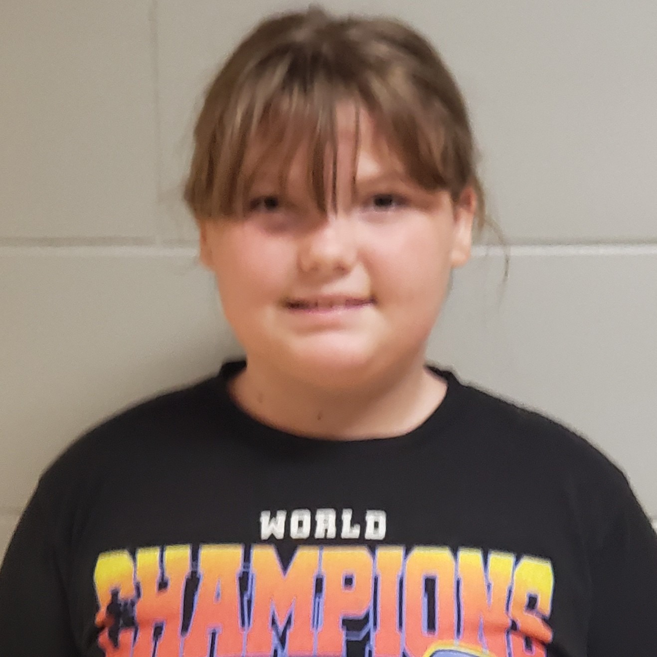 smiling girl with light brown hair pulled back wearing a black World Champions t-shirt