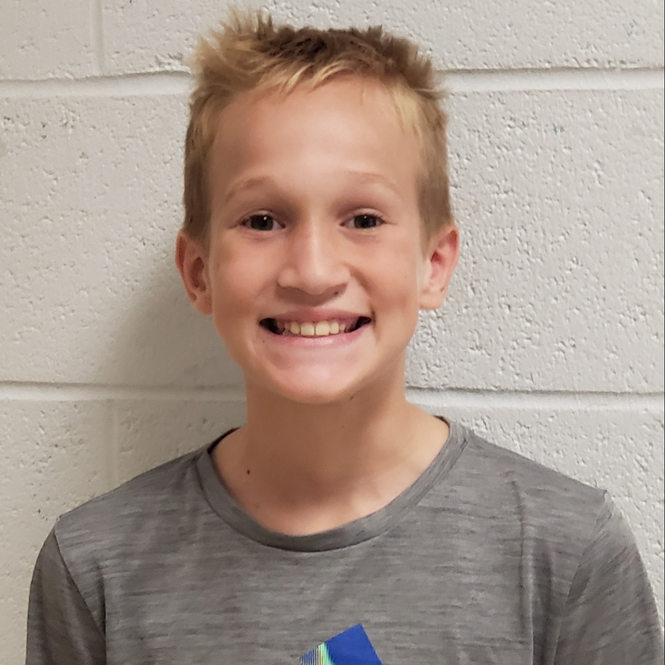 smiling boy with blonde spiky hair wearing a gray t-shirt