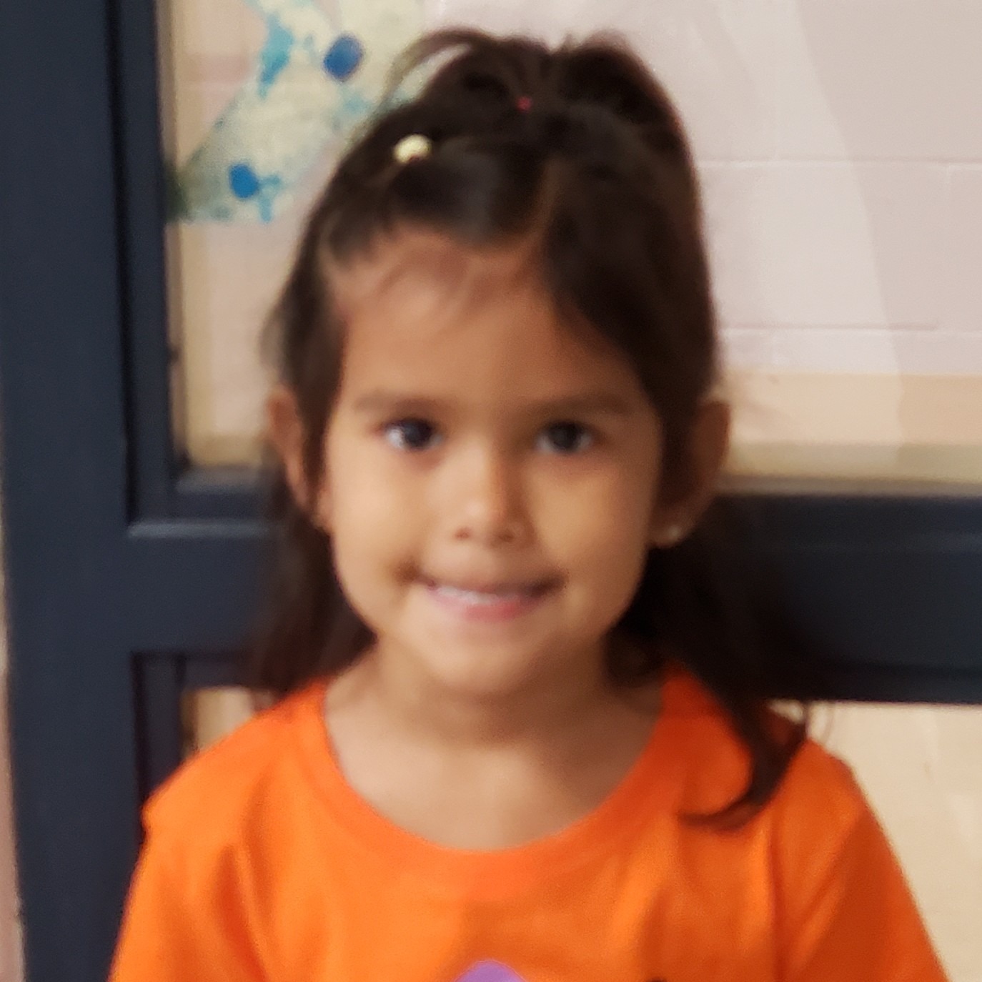 little girl with dark hair pulled up wearing an orange t-shirt